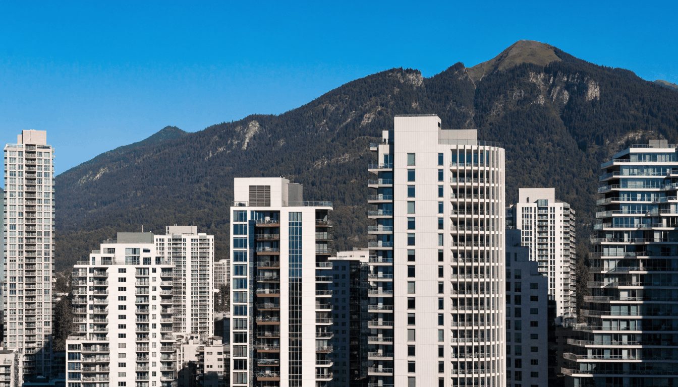 Vancouver-style skyline showing modern high-rise condominiums with a mountain backdrop under clear blue sky, characteristic of the Canadian short-term rental market.